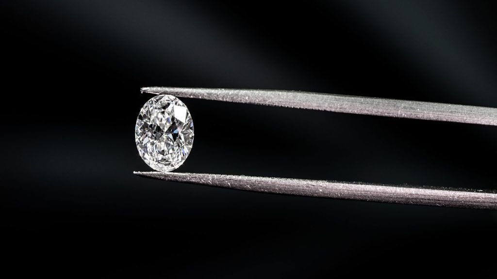 diamond held between tweezers in front of a black background