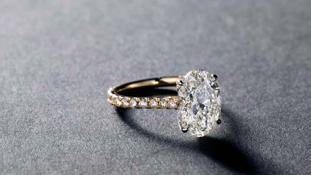 yellow gold diamond encrusted oval diamond ring on grey table